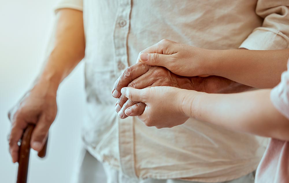 A person holds the hand of an elderly individual who is using a cane, reflecting a touching moment in senior living in Illinois.